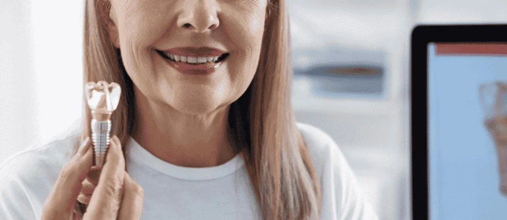 Smiling woman holding a dental implant model